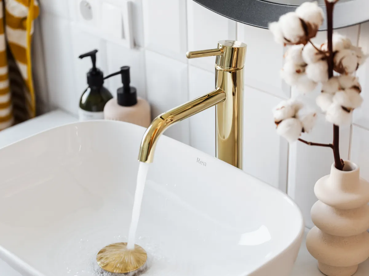 Mitigeur doré avec eau courante au-dessus d’une vasque blanche dans une salle de bains lumineuse