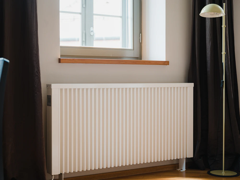 Radiateur électrique blanc moderne sous une fenêtre dans un intérieur lumineux avec parquet